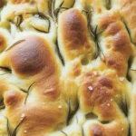 Freshly baked focaccia bread topped with rosemary and sea salt, showcasing its golden texture.
