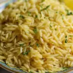 Delicious lemon orzo dish garnished with herbs and lemon slices.